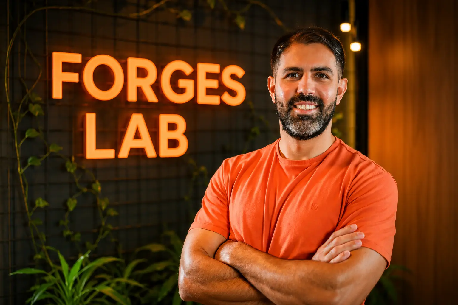 Diogo, fundador da Forges Lab, de braços cruzados diante do letreiro laranja da marca